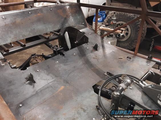 Custom off-road vehicle chassis with metal floor panels and roll cage. Another vehicle is visible in the background