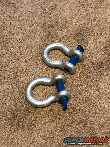 Two silver tow shackles with blue pins on carpet
