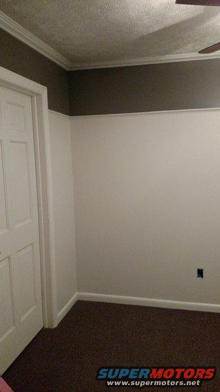 Interior room with white door, brown carpet, and white walls with a dark gray accent