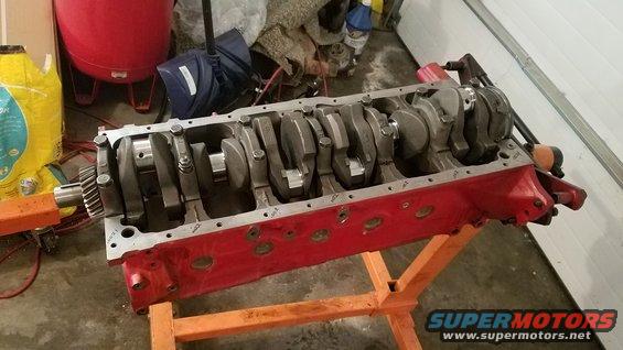 Red engine block with crankshaft and connecting rods visible, mounted on an orange engine stand