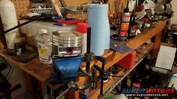 Workbench with a piston in a vise, mineral oil, paper towels, and various tools and automotive fluids