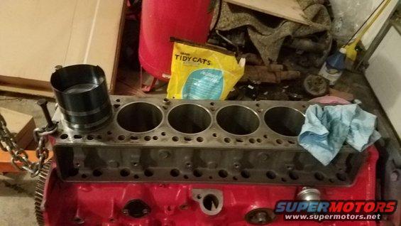 Engine block with five cylinders and a piston ring compressor tool on top. A bag of Tidy Cats litter is in the background