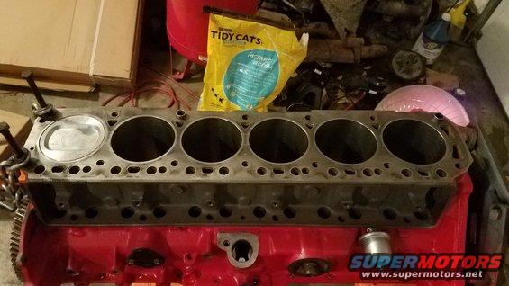 Engine block with one piston installed, sitting on a red base. Bag of Tidy Cats litter in background