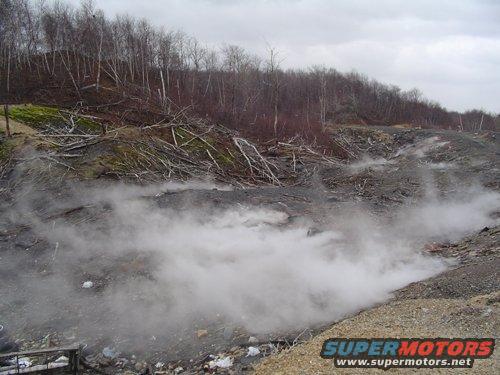 Desolate landscape with steam rising from the ground and trees in the background
