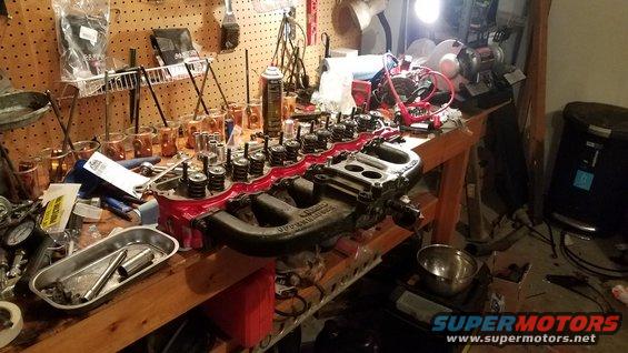 Engine cylinder head and intake manifold on a workbench with tools and parts