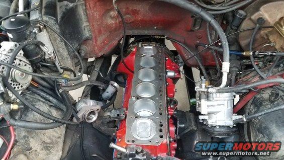 Engine bay with engine block disassembled, showing cylinders and gasket. Wires and hoses are visible