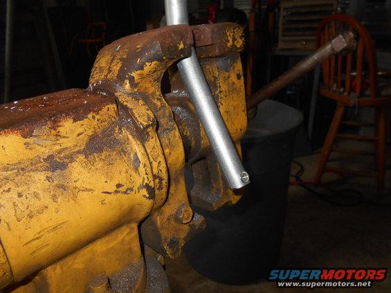 Close-up of a rusty yellow vice holding a silver pipe.