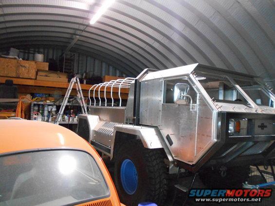 Custom silver vehicle in a garage with an orange car in the foreground.