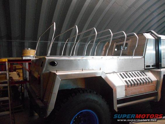 Custom-built vehicle with brushed metal body and roll cage in a metal building.