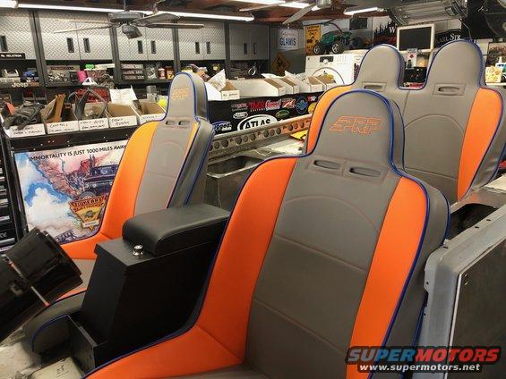 Two PRP racing seats with orange and gray upholstery and a black center console.