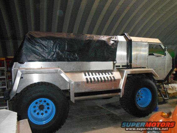 Custom aluminum truck with large tires and black tarp covering the rear.