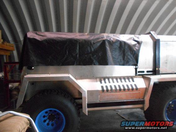 Custom aluminum truck bed cover on a vehicle with large off-road tires and blue rims.