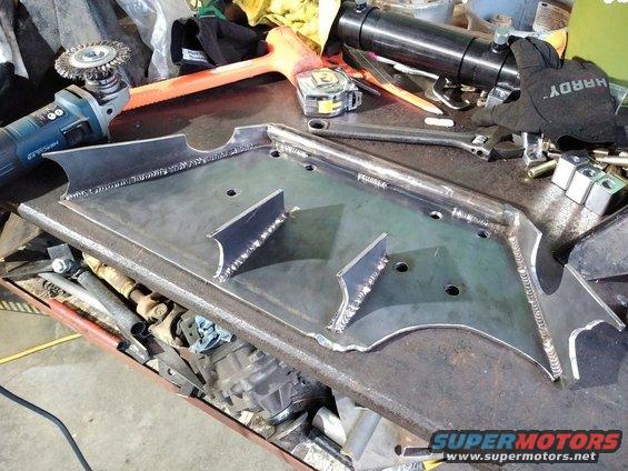 Fabricated metal part with welds and mounting holes on a workbench, next to tools