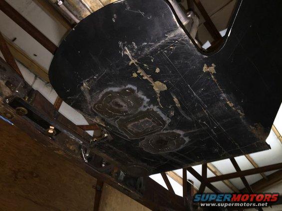 underside of a black vehicle part with scuffs and some patched areas, mounted on metal supports