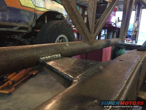 Welded metal frame with a large tire and part of a colorful vehicle in the background