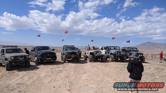 Several SUVs parked on dirt road with blue sky and clouds