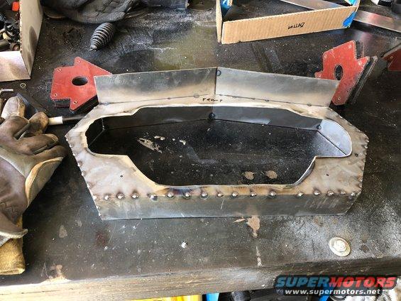Metal fabrication with 'FRONT' written on it, on a workbench with welding magnets and gloves