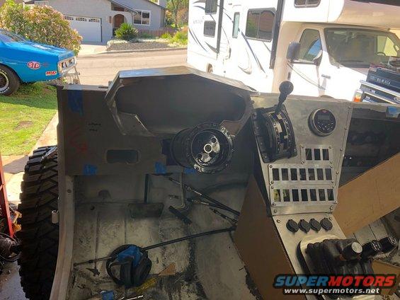 Vehicle interior with exposed metal dashboard, steering column, and gear shifter. Tools and wiring are visible