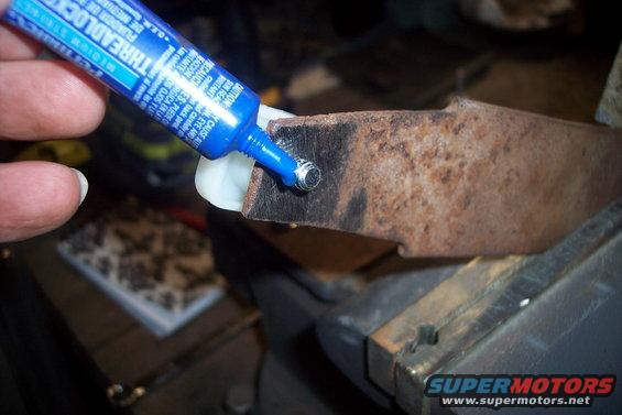 Tube of blue threadlocker being applied to a rusty metal object held in a vise