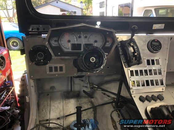Custom dashboard with aftermarket gauges, speakers, and a row of switches. A shifter is visible. The interior appears to be a work in progress