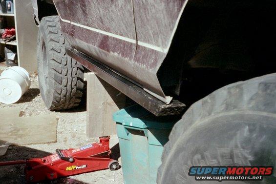 close-up of vehicle's side panel, large off-road tires, and a red hydraulic jack on the ground