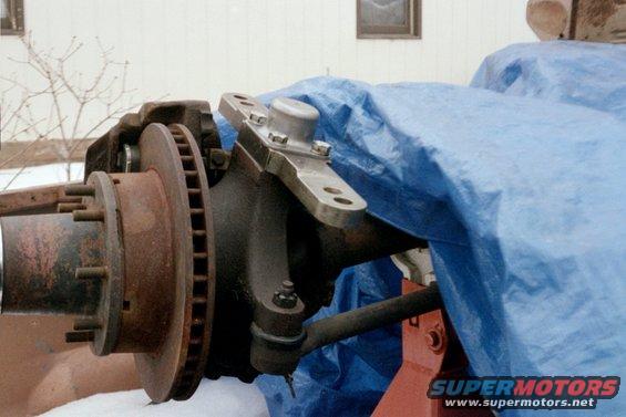 Close-up of rusty brake rotor and steering linkage components, partially covered by a blue tarp