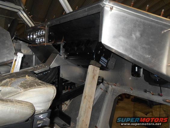 Interior of a vehicle build with custom aluminum dash, gauges, blower motor, and worn seat.
