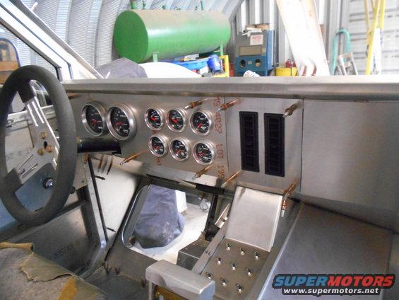 Custom vehicle dashboard with gauges, steering wheel, and vents in a workshop.