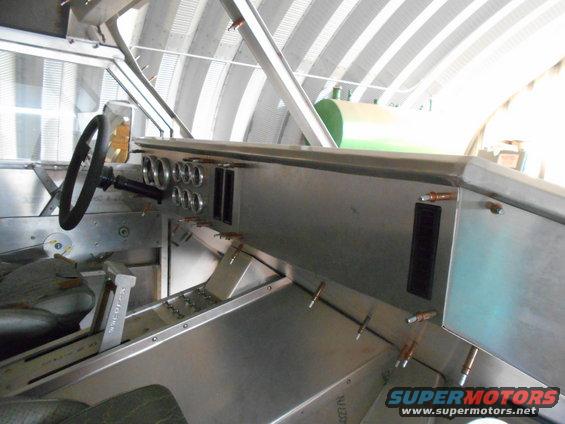 Interior of a custom vehicle with metal dashboard, gauges, steering wheel, and gear shifter.
