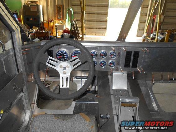 Interior of a custom vehicle with metal dashboard, gauges, steering wheel, and shifter.