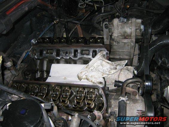 Engine with valve covers removed, showing rocker arms and intake manifold. A white cloth covers part of the engine