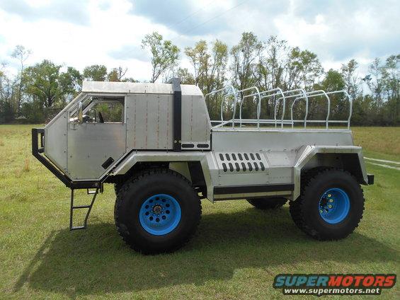 Custom off-road vehicle with silver body panels and blue wheels parked on grass