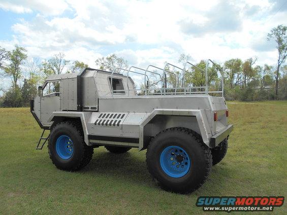 Custom truck with big tires and blue rims, parked on grass