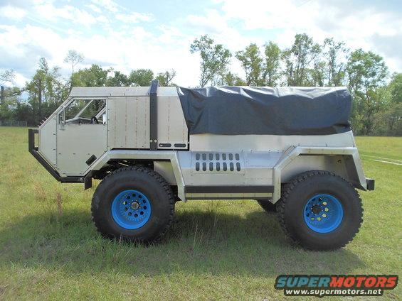 Side view of custom off-road truck with blue wheels and a black tarp cover