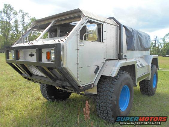 Custom-built truck with aluminum body panels and blue wheels parked in a grassy field