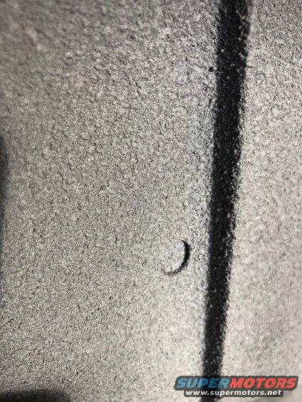 Close-up of a gray textured surface with a black line and a small crescent-shaped indentation. Supermotors.net logo visible