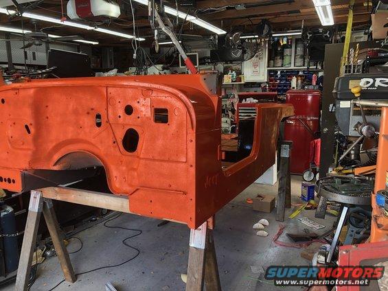 Orange Jeep tub on sawhorses in a garage, undergoing restoration