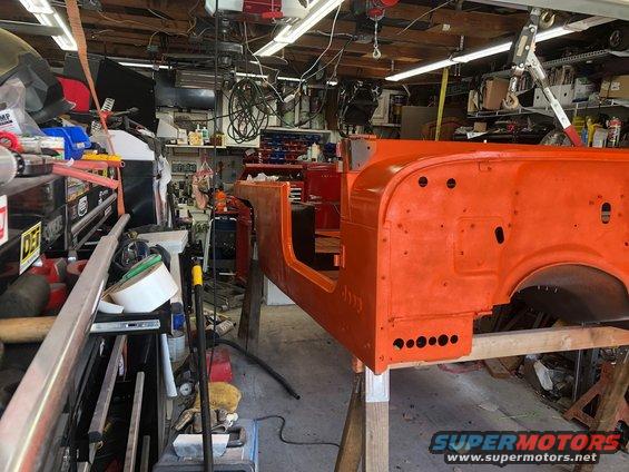 Orange Jeep Wrangler body on sawhorses in a garage, undergoing restoration