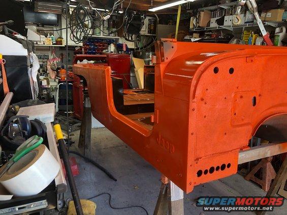 Orange Jeep tub body, sans doors and fenders, on sawhorses in a garage. 'Jeep' is embossed on the side