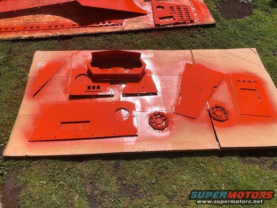 dashboard components and other car parts laid out on cardboard, being spray painted orange