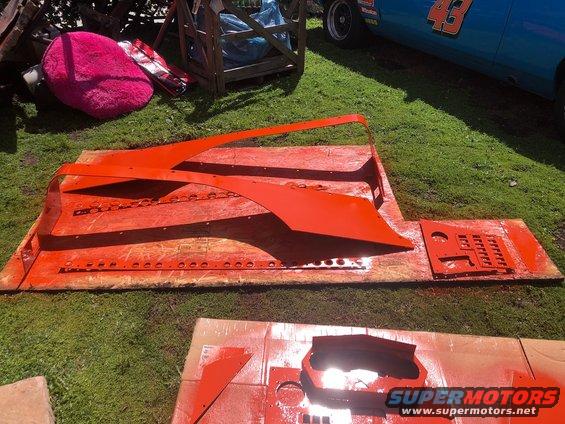 Orange painted Jeep Wrangler fender and other body panels laid out on plywood and grass