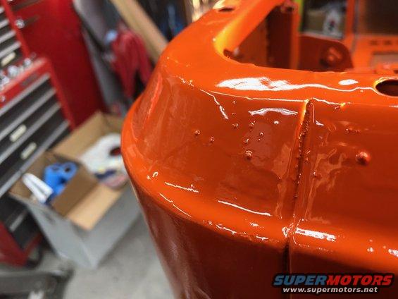 Close-up of an orange painted metal part with visible paint imperfections and a Supermotors.net watermark