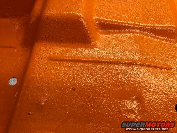 Orange painted metal floor pan with textured surface and raised ribs. A circular hole is visible on the left