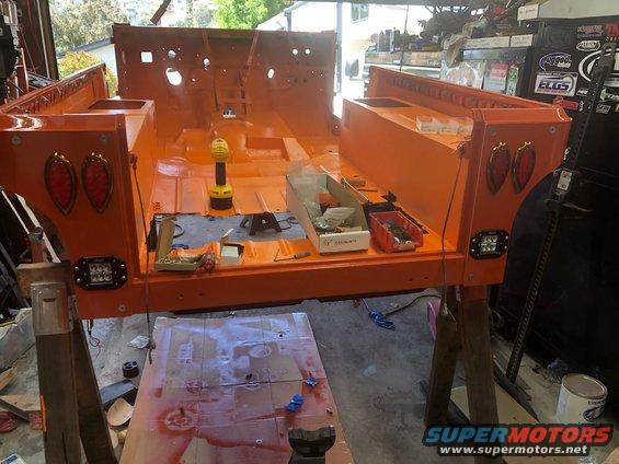 Orange Jeep CJ/YJ tub on sawhorses, showing rear taillights and LED pods