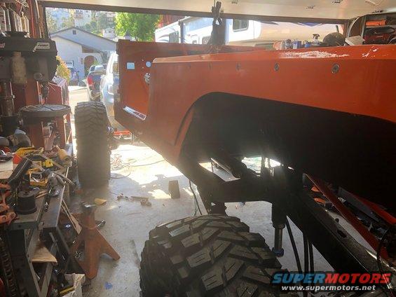 Orange Jeep CJ-7 body on jack stands in a garage, undergoing work. Big off-road tires are visible