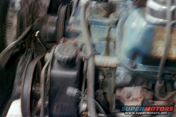 Engine block with belts, pulleys, and fluid reservoir. Blue and black components are visible