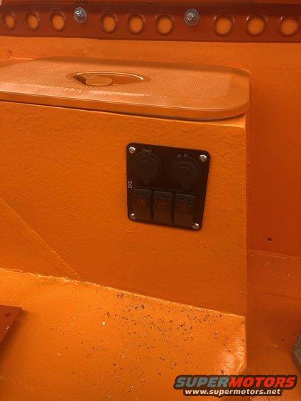 Close-up of an orange interior panel with a black electrical switch and power outlet assembly