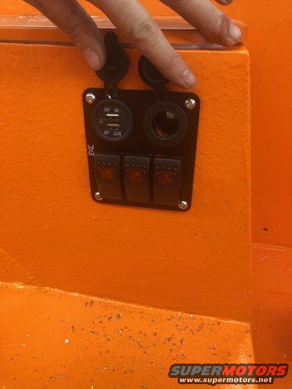 Orange dashboard panel with three red-lit switches and two USB ports, one covered