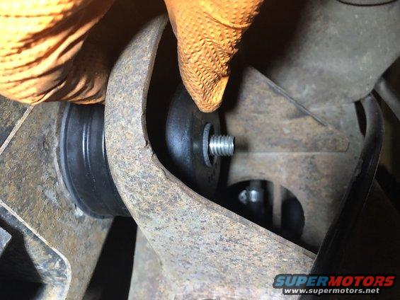 Gloved hand installing a bolt through a rubber bushing on a rusty suspension component
