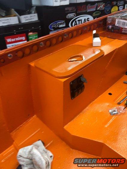 Orange-painted truck bed interior with wheel well storage box and outlet